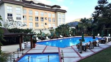 A hotel with a swimming pool, outdoor seating, and a building with multiple windows.