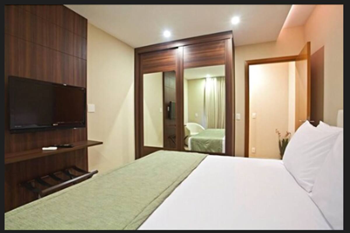 Ein Hotelzimmer mit einem Bett, einem an der Wand montierten Fernseher, einem Kleiderschrank und einem Spiegel.