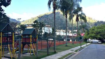 A playground with swings and climbing structures, a road, and a hill with trees in the background.