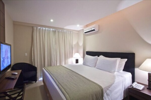 A hotel room with a bed, a desk with a computer, a television, and an air conditioning unit. - Hotel Granja Brasil Resort (Petrópolis)