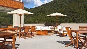 An outdoor patio with wooden furniture, white cushions, and umbrellas, overlooking a forested hillside. - Hotel Granja Brasil Resort (Petrópolis)