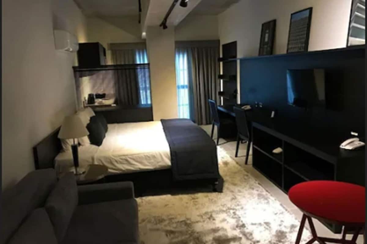 Ein Hotelzimmer mit Bett, Schreibtisch, Stuhl, Fernseher und einem roten Hocker.