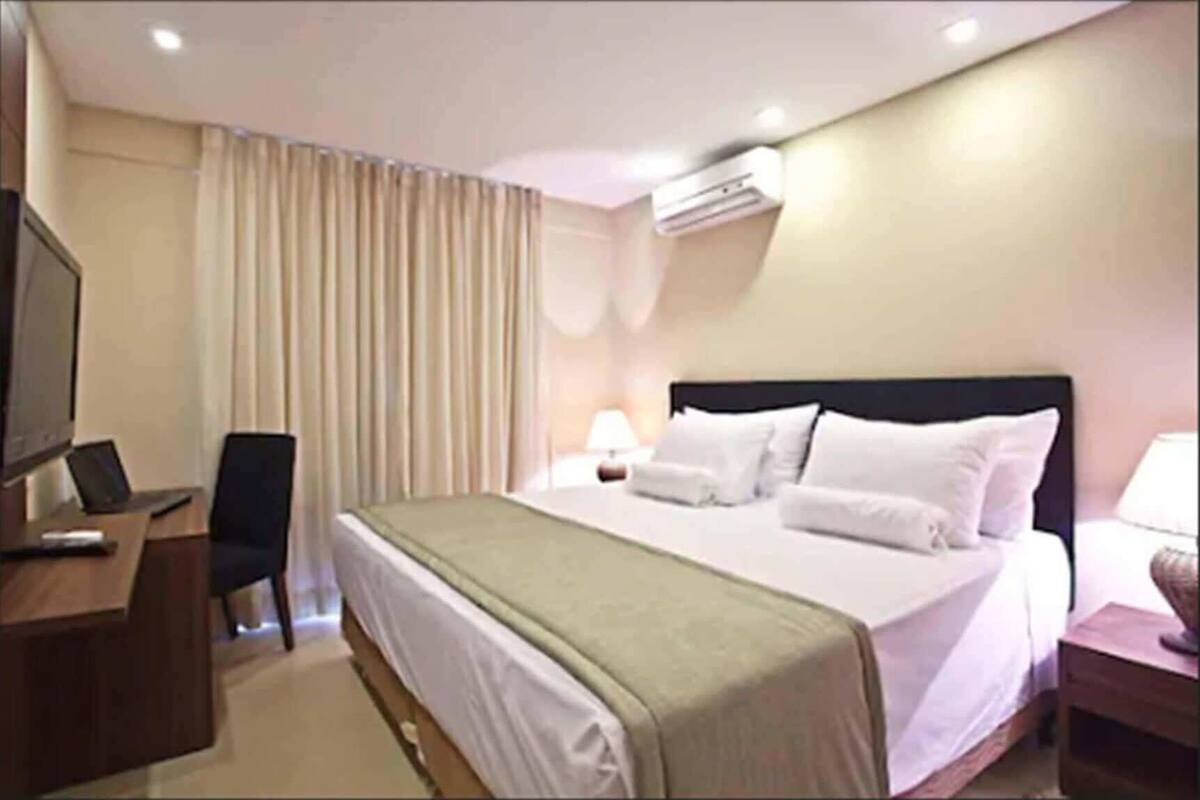 Ein Hotelzimmer mit Bett, Schreibtisch, Stuhl, Klimaanlage und Fernseher.