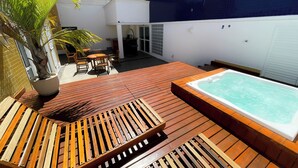Una terraza de madera con un jacuzzi, mobiliario exterior y una planta en maceta.