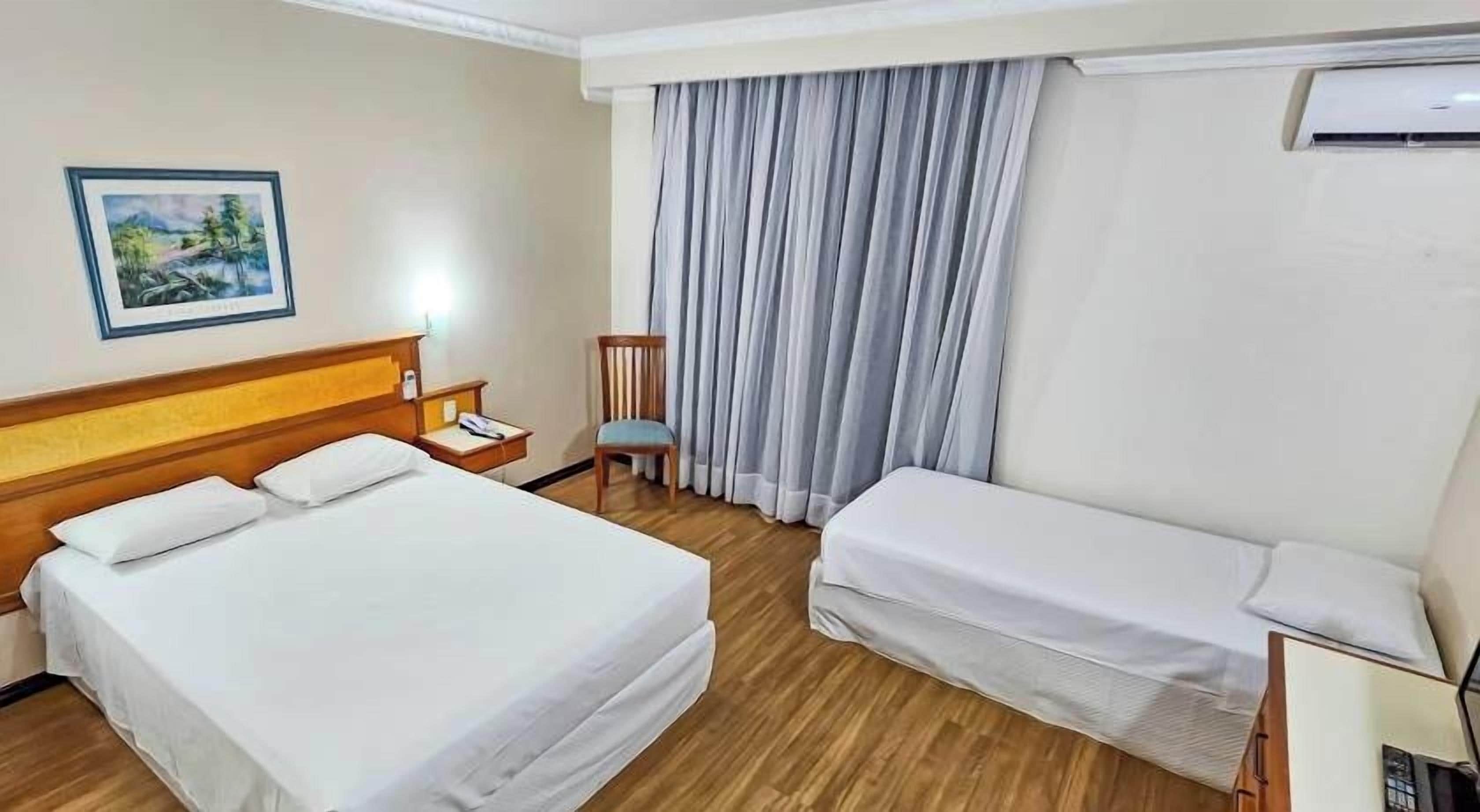 A hotel room with a double bed, a single bed, a nightstand, a chair, and a painting on the wall.