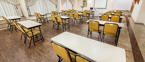 A conference room with multiple tables and chairs, a whiteboard, and a projector screen.