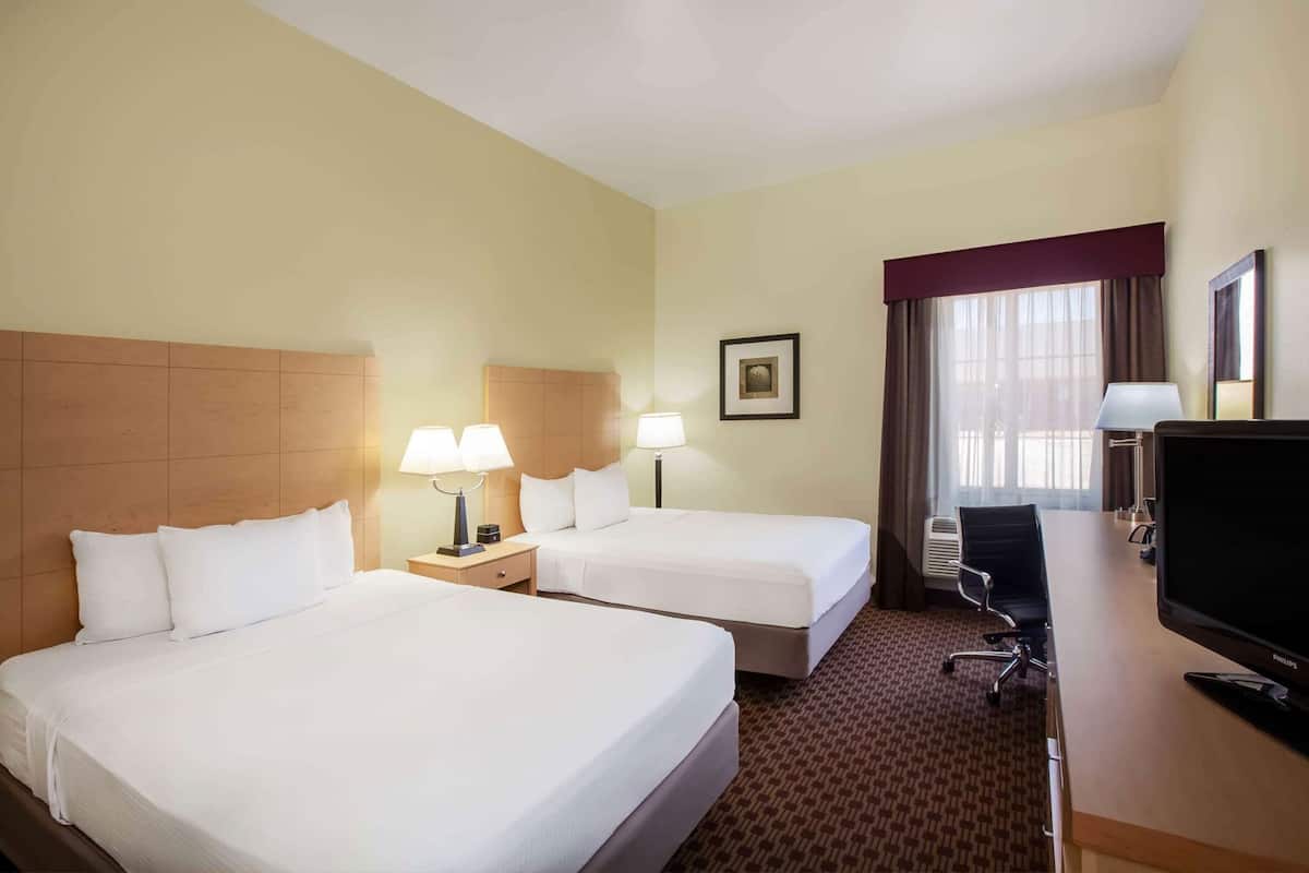 Hotelkamer met twee bedden, een bureau met computer, een stoel, een televisie en een raam met gordijnen.