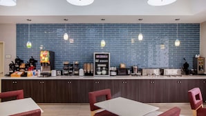Ett modernt köksområde med ett blått kakel på väggen bakom arbetsbänken, hängande taklampor och en mängd olika apparater, inklusive en kaffemaskin och en mikrovågsugn.