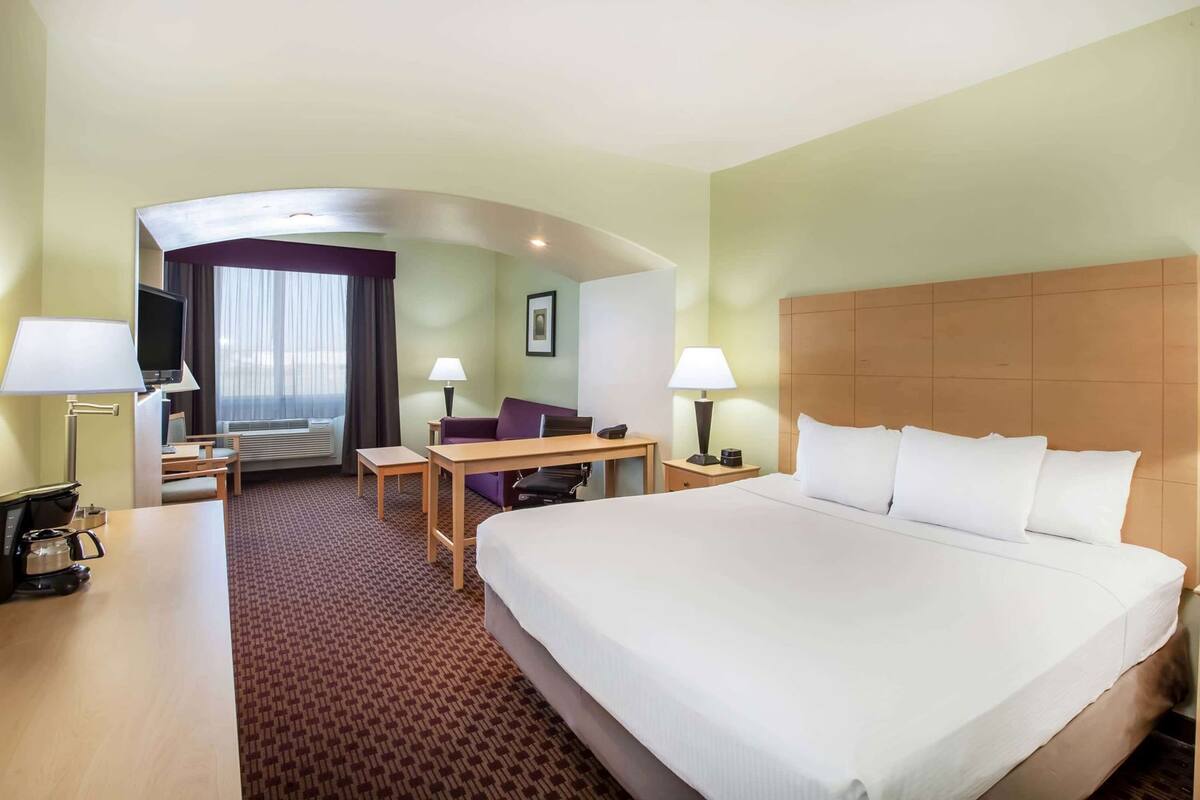 Een hotelkamer met een groot bed, een bureau, een stoel, een televisie en een raam met gordijnen.