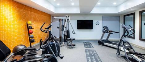 A gym with various exercise equipment, a treadmill, and a wall-mounted TV.