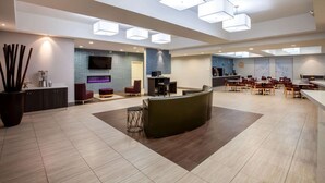 En rymlig entréhall med modern design, med en sittgrupp bestående av soffor och fåtöljer, ett köksområde och en stor platt-TV som är monterad på väggen.