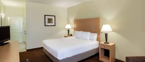 A hotel room with a large bed, two bedside tables with lamps, a television, and a patterned carpet.
