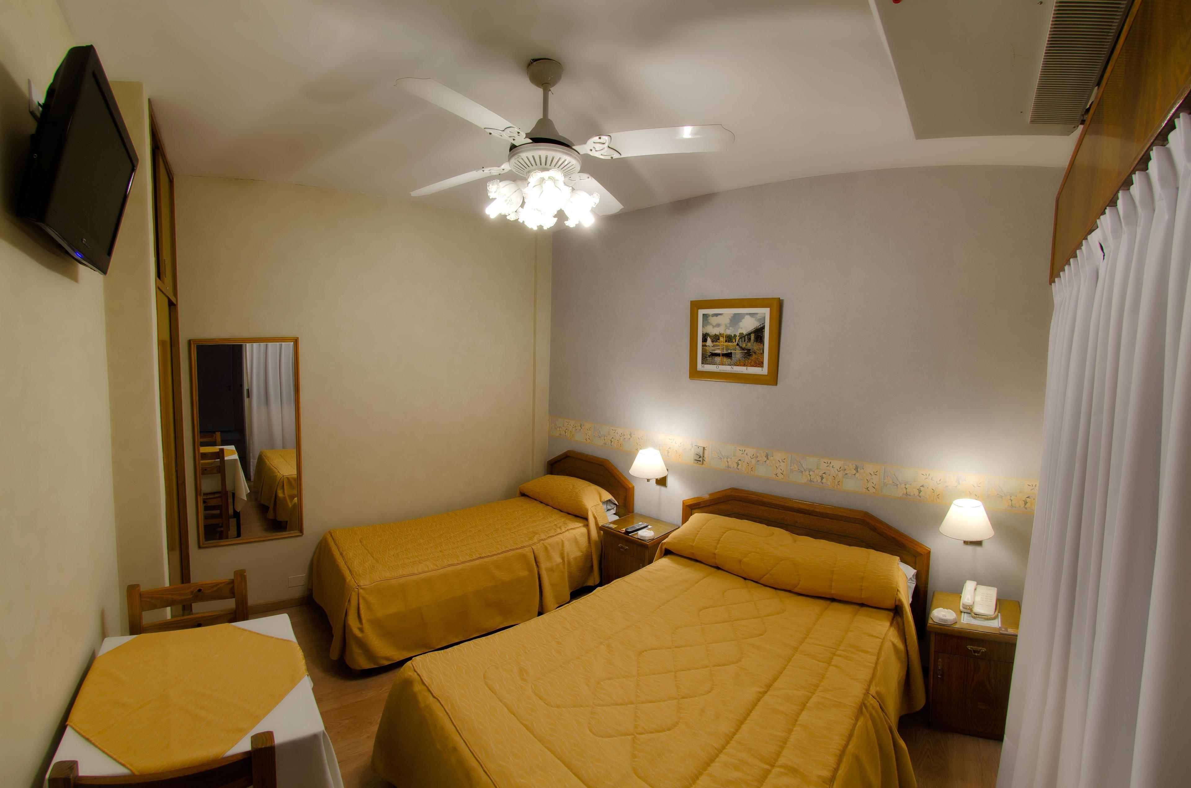 Habitación de hotel con dos camas, ventilador de techo, televisor, escritorio y una silla.