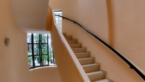 A curved staircase with beige walls and black handrails, leading to a landing with a window overlooking greenery. - Hotel Internacional (Buenos Aires)