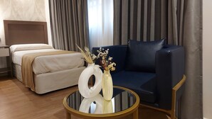 A hotel room with a bed, a sofa, a round glass coffee table with a vase, and curtains. - Hotel Internacional (Buenos Aires)