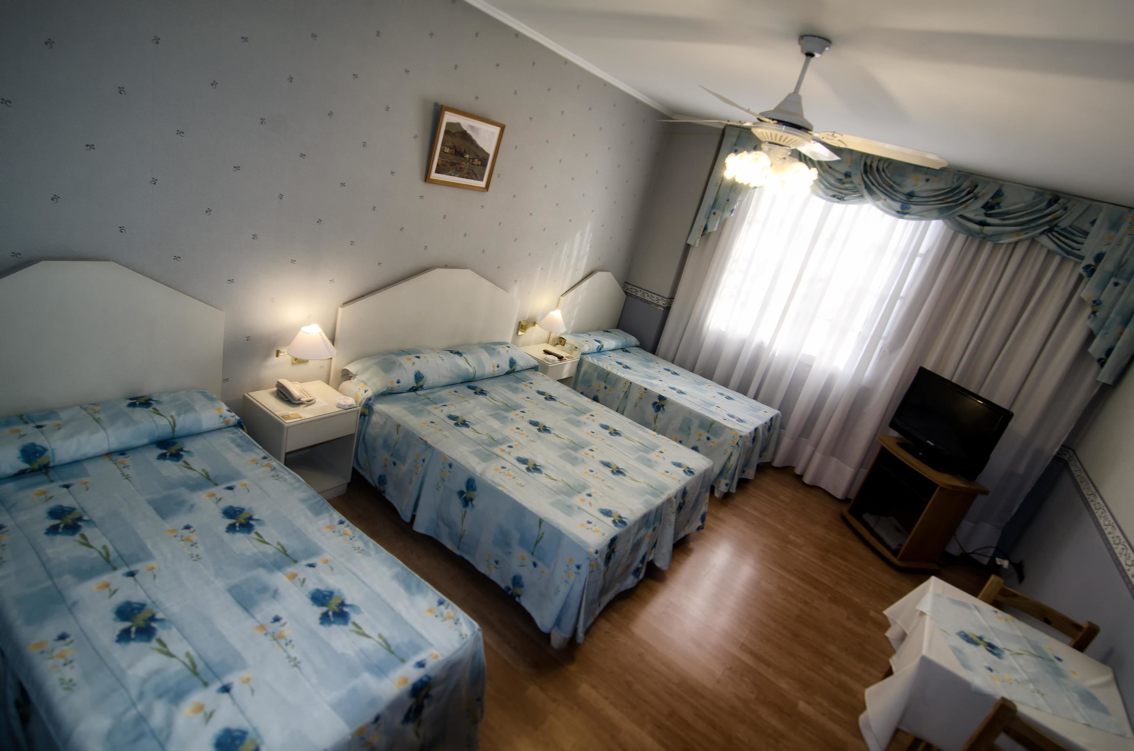 A hotel room with three single beds, a ceiling fan, a television on a wooden stand, and a small table with a map.