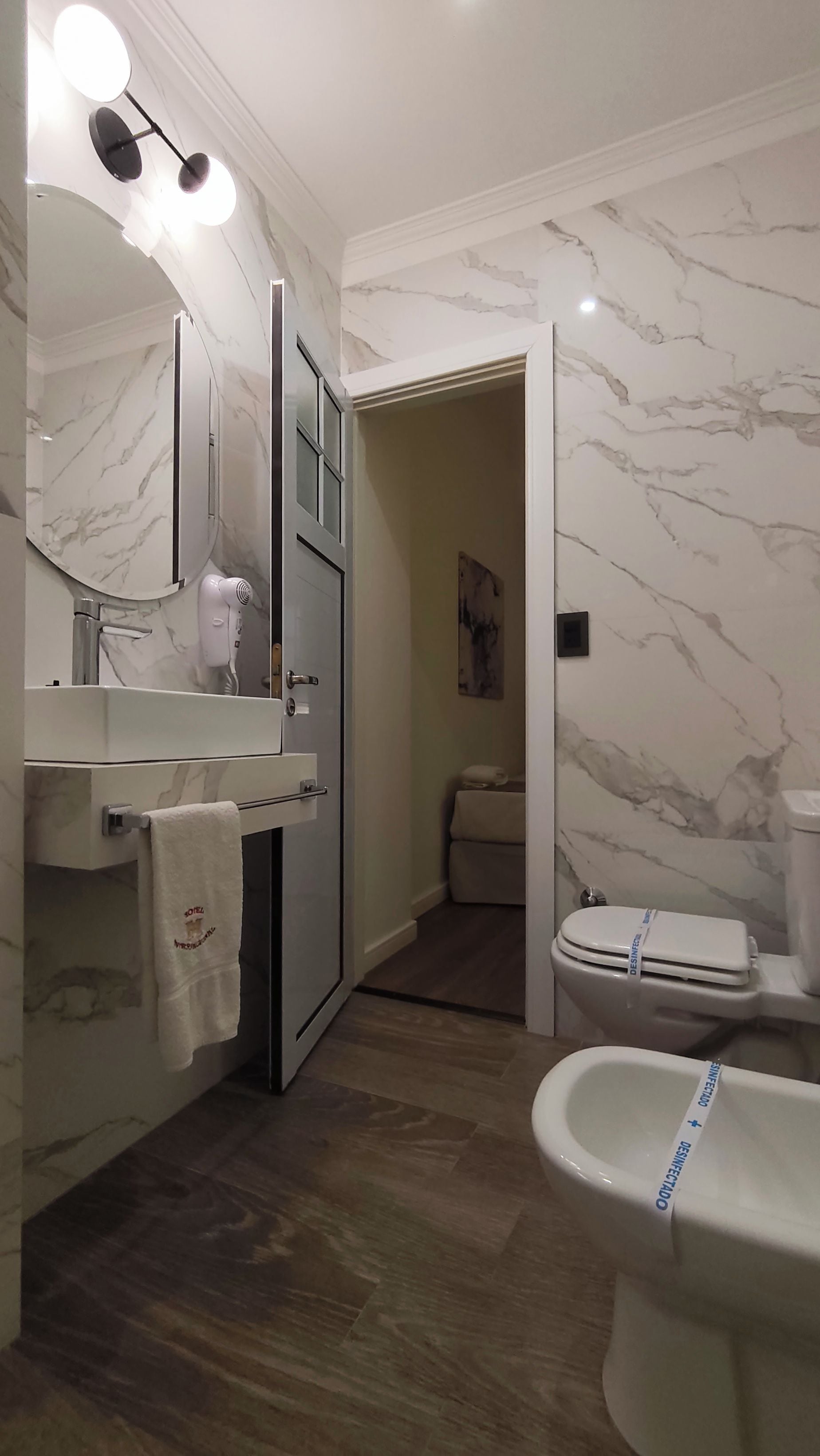 Une salle de bain avec un mur en marbre, un lavabo, un miroir, une serviette, des toilettes et un bidet.