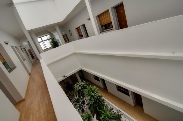 Un interior de varios niveles con un atrio central, piso de madera y plantas en macetas.