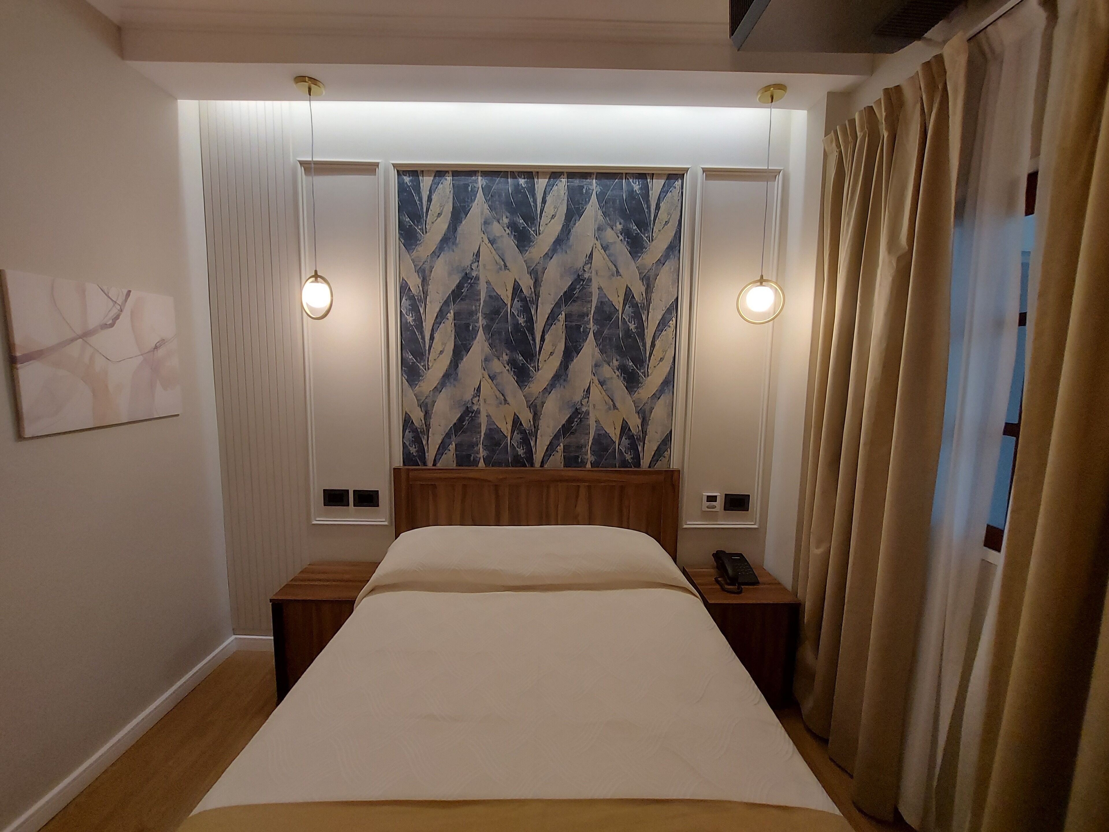 A hotel room with a large bed, two bedside tables, a wall-mounted telephone, and a patterned tapestry above the bed.