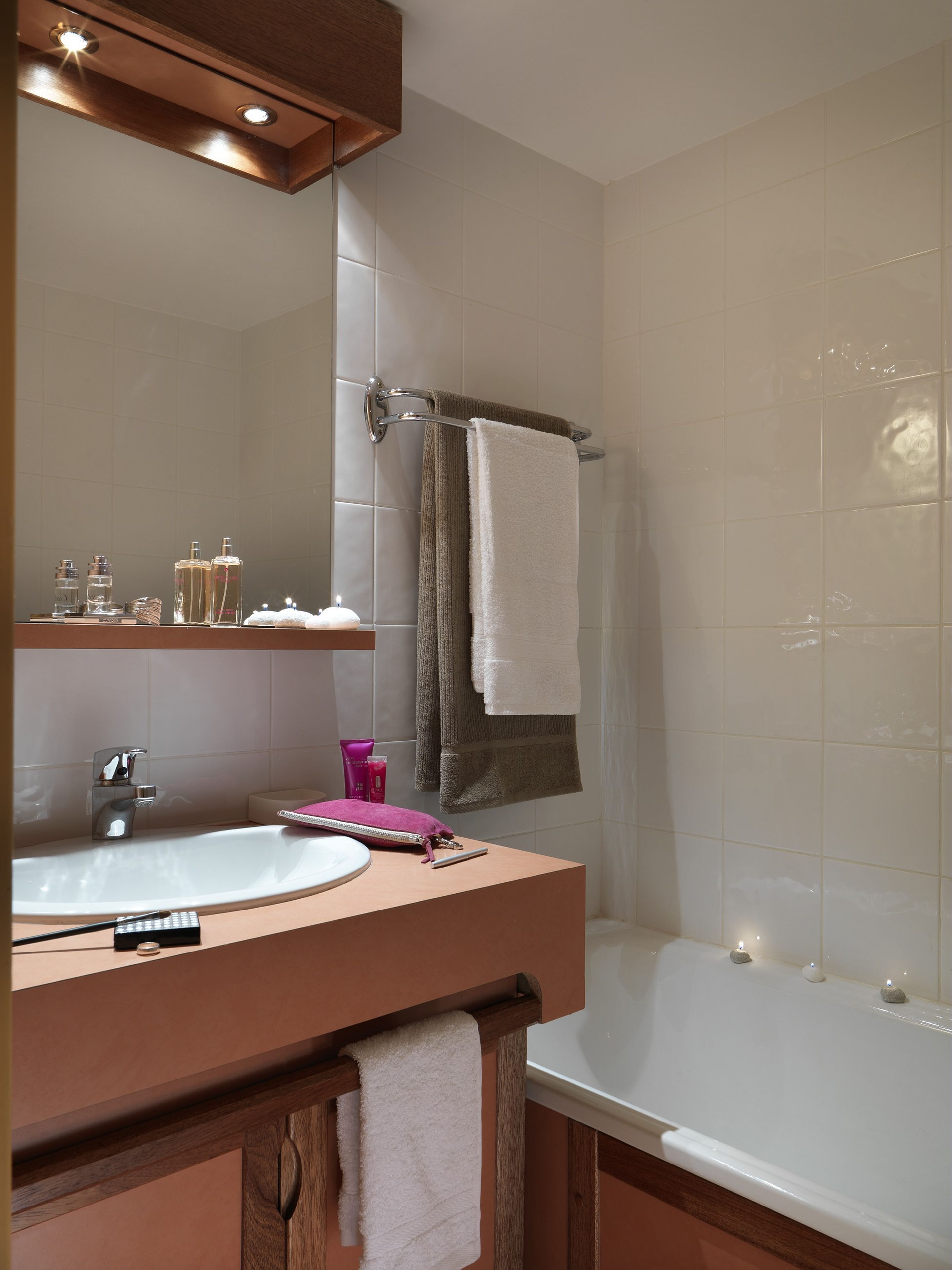 A bathroom with a sink, mirror, and bathtub. There are toiletries on the sink and a towel rack above the bathtub.