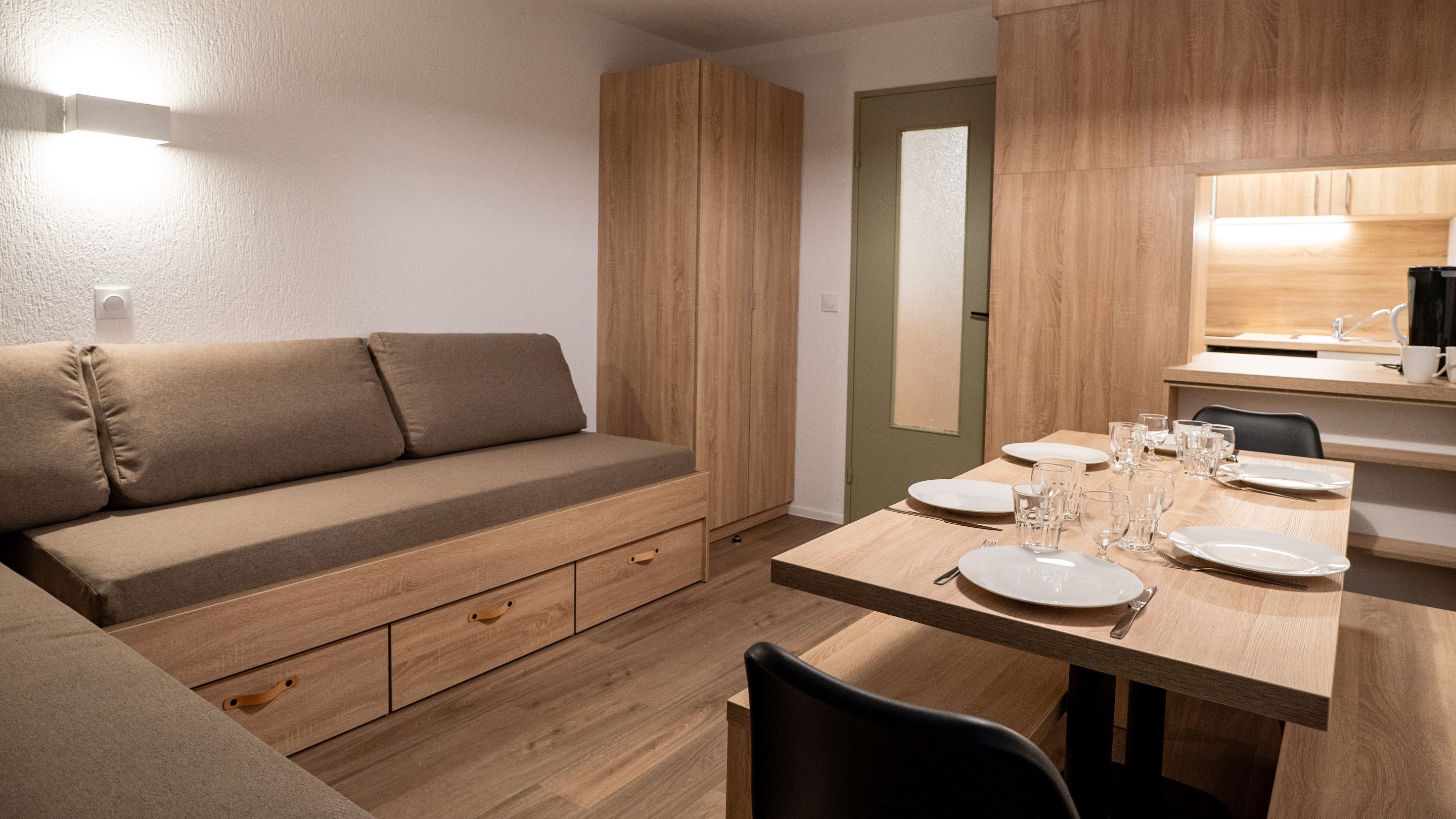 A modern, compact living space with a sofa, a dining table set for four, and a kitchenette area.