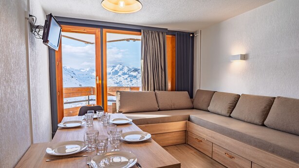 Una habitación moderna con una mesa de madera para cuatro comensales, un sofá y un amplio ventanal con vistas a la montaña.