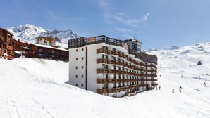 Un hotel moderno con varios pisos, pistas de esquí y un paisaje de montaña al fondo.
