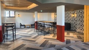 Un interior moderno con suelo de espiga, una zona de comedor central con mesa y sillas de madera, y una pared con estampado geométrico.