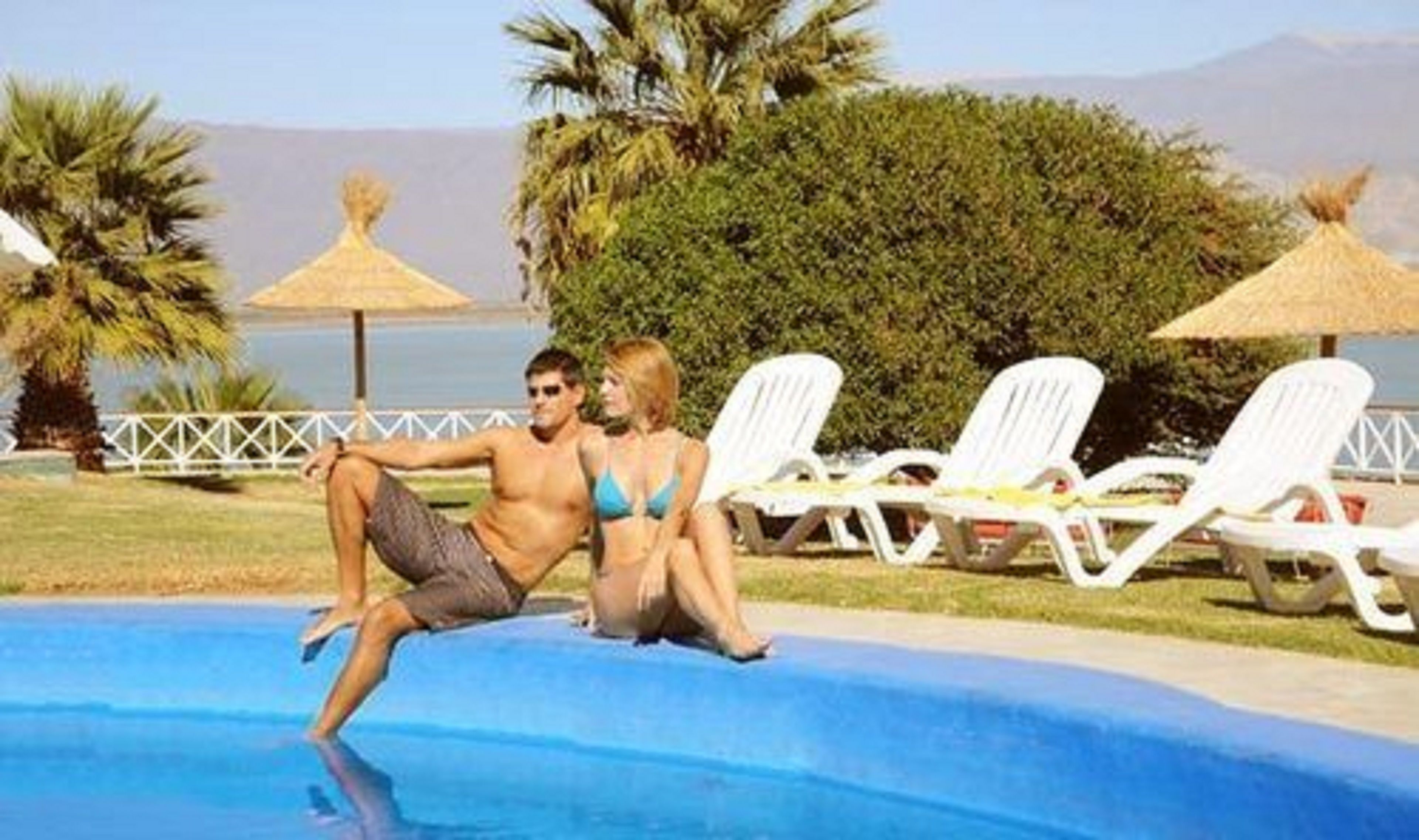 Zona de piscina con sillas de descanso y vista al mar.