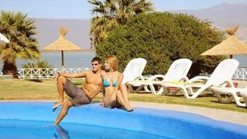 Zona de piscina con sillas de descanso y vista al mar.