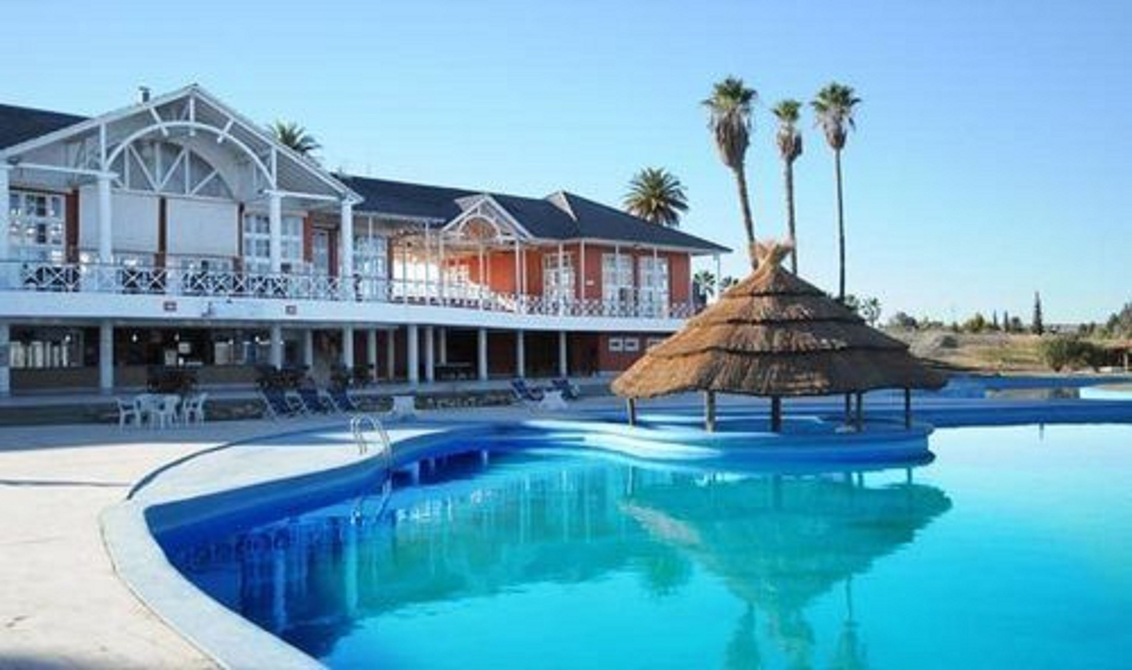Un hôtel doté d’une piscine, d’une structure à toit de chaume et de palmiers.