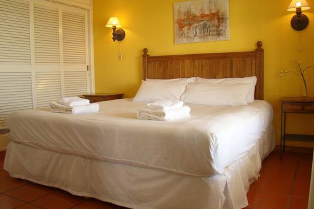 A neatly made bed with white linens and towels, a wooden headboard, and two wall-mounted lamps.