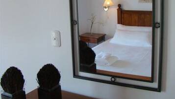 A hotel room with a large mirror, a wooden headboard, a bedside lamp, a small wooden nightstand, and two decorative vases on a wooden dresser.