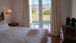 A hotel room with a bed, a nightstand, a lamp, and a view of a grassy area and a body of water through a glass door. - Del Bono Beach (San Juan)
