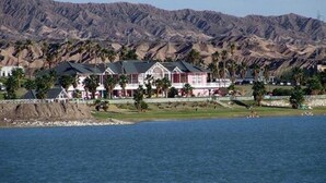 A large, multi-story building with a prominent red and white facade, situated near a body of water with mountains in the background. - Del Bono Beach (San Juan)