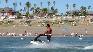 A person jet-skiing on a beach with palm trees and beach umbrellas in the background. - Del Bono Beach (San Juan)