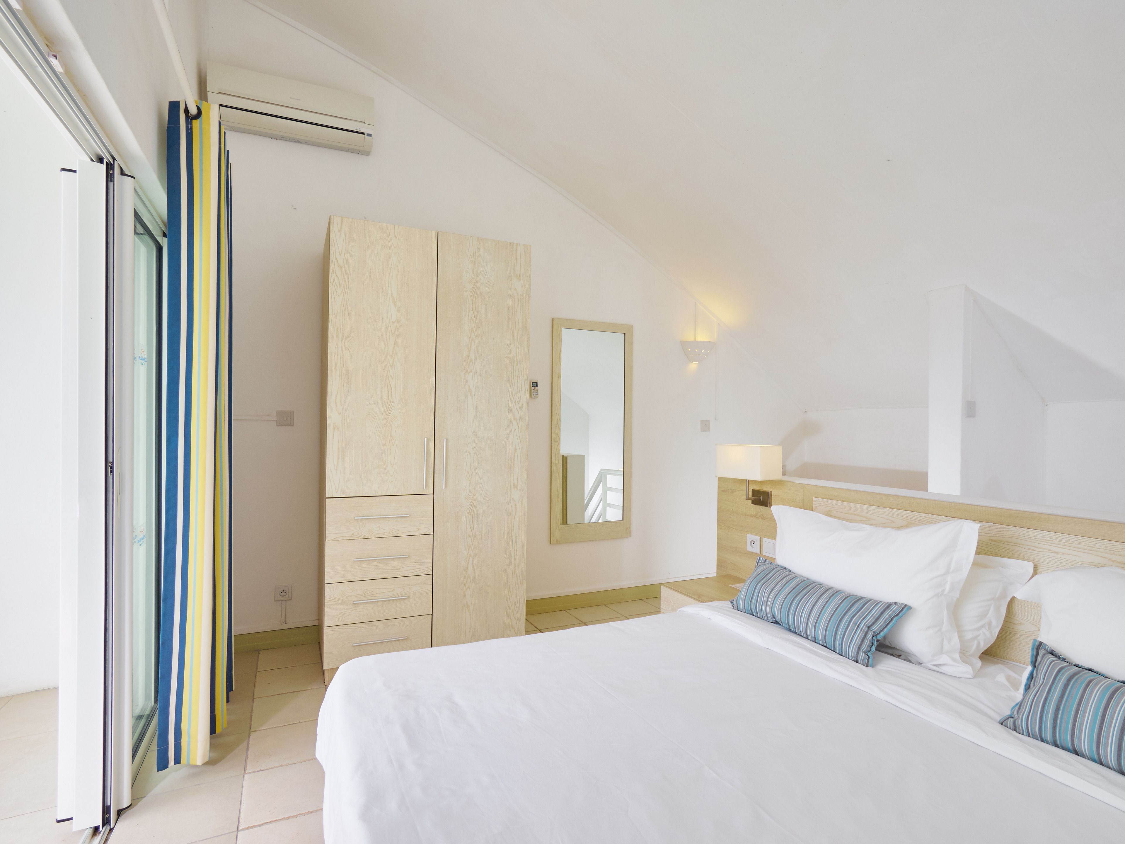 A hotel room with a bed, a wardrobe, a mirror, and a window with curtains.