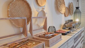 A buffet setup with wicker baskets and wooden serving boards, a hanging lantern, and a tiled floor. - Le Beachclub Serviced Apartments and Villas (Grand-Baie)