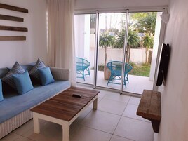 Una sala de estar con un sofá, una mesa de centro y un ventanal corredizo que da a un espacio exterior con sillas y una mesa.