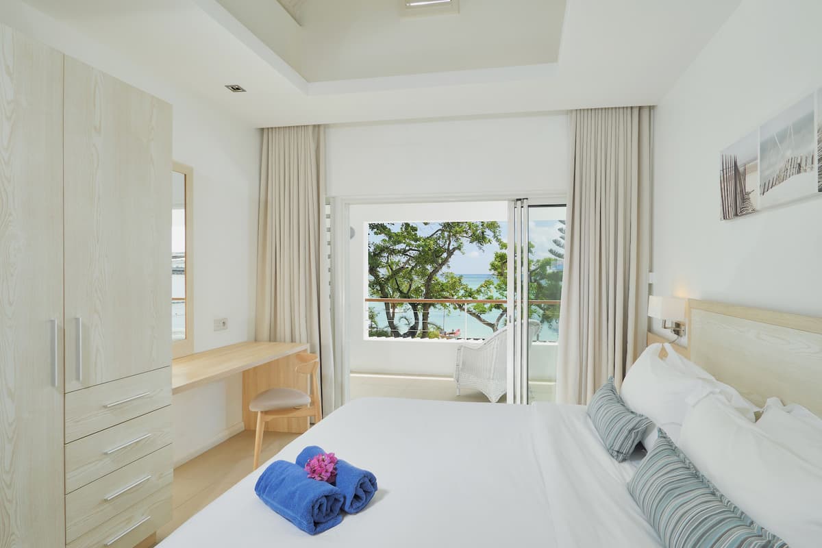 A hotel room with a bed, a desk, a chair, and a balcony with a view of the sea.