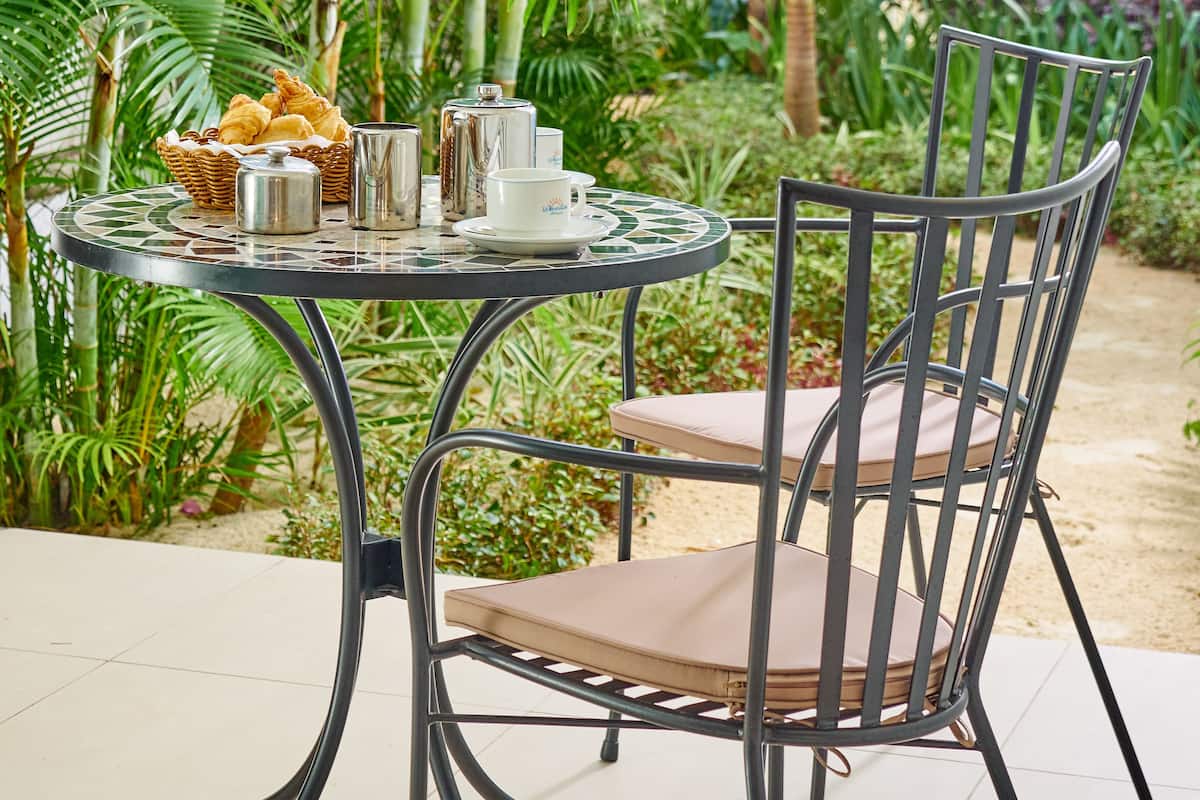A round metal table with a cushioned chair, surrounded by lush green plants.