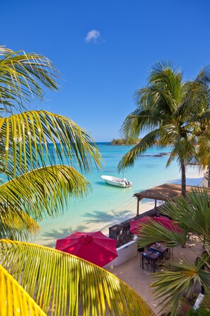 Vista de la playa con un bote, palmeras y una sombrilla.