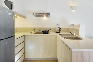 Una cocina compacta con un refrigerador de acero inoxidable, estufa integrada, un lavamanos y una lámpara sobre la encimera.