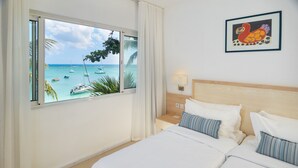 A hotel room with a bed, a nightstand, a lamp, and a window with a view of the sea and boats. - Le Beachclub Serviced Apartments and Villas (Grand-Baie)