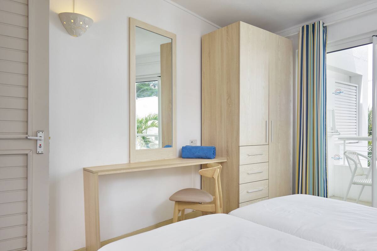 A bedroom with a bed, a desk with a chair, a wardrobe, and a window with curtains.