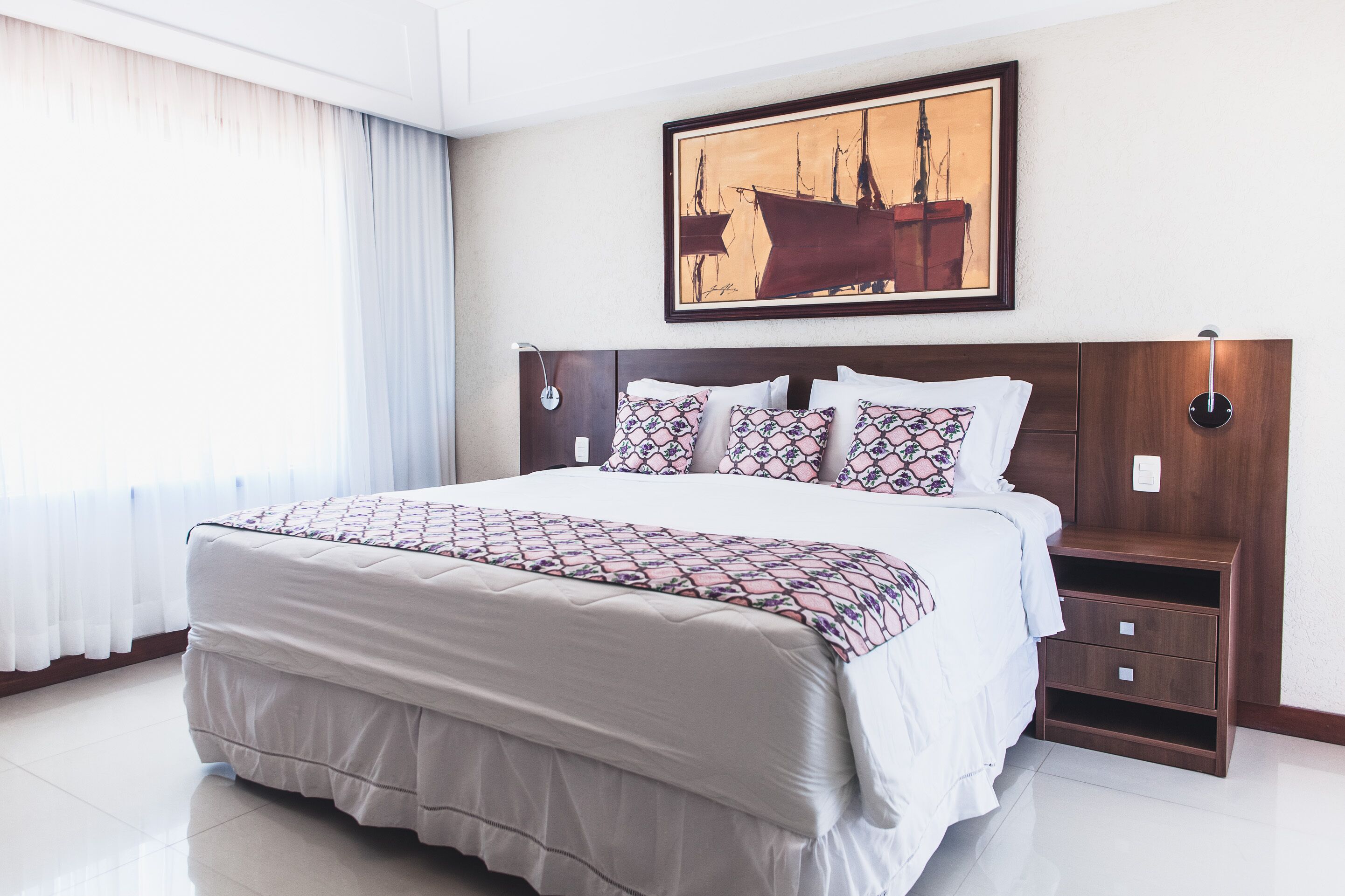 A neatly made bed with a patterned bedspread, a headboard with a framed artwork, and a bedside table with a lamp.
