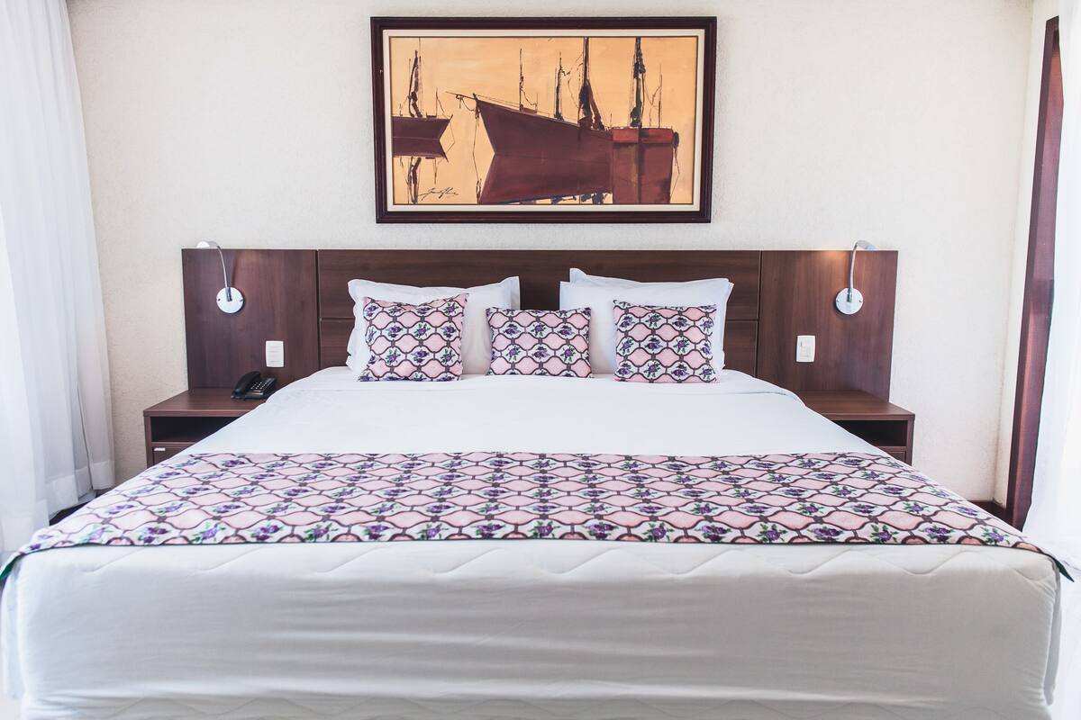 Une chambre d’hôtel avec un grand lit, une tête de lit agrémentée d’une œuvre d’art encadrée, deux tables de chevet et une petite table d’appoint.