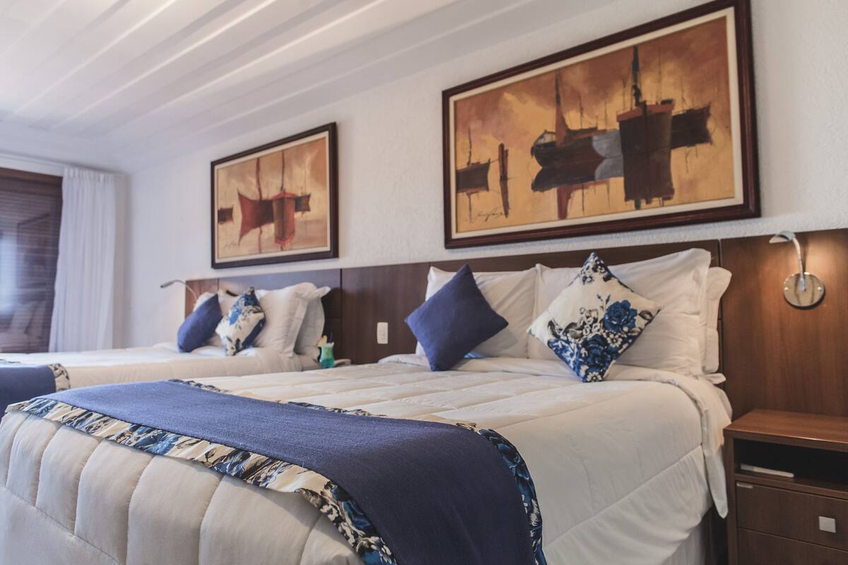 Une chambre d’hôtel avec deux lits, une tête de lit en bois et des œuvres d’art accrochées aux murs.