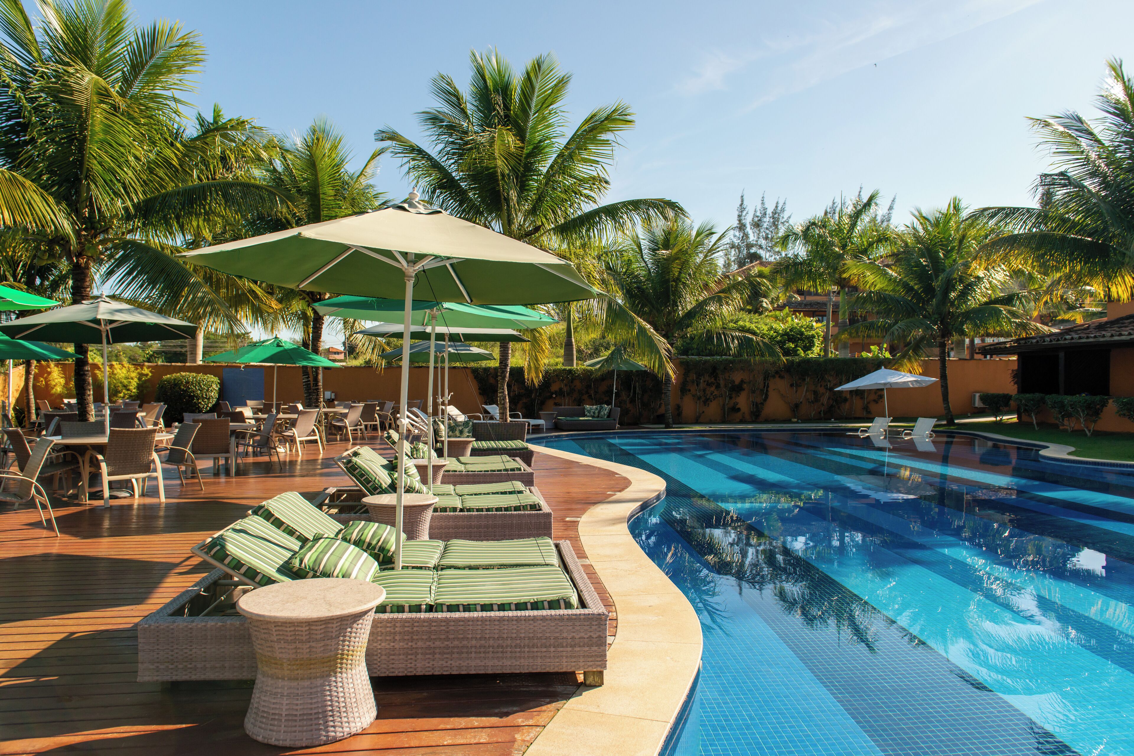 A poolside area with lounge chairs and umbrellas, surrounded by palm trees.