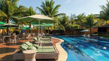 A poolside area with lounge chairs and umbrellas, surrounded by palm trees.
